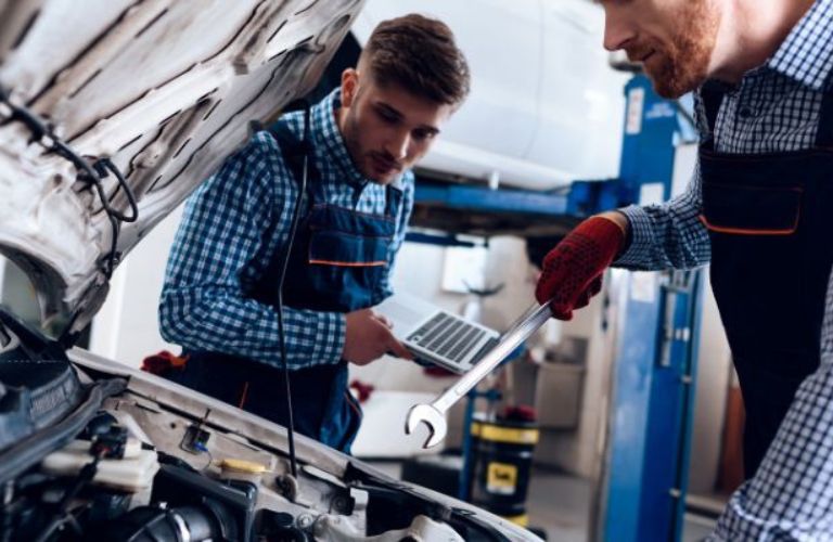 two technicians working under the hood of a car