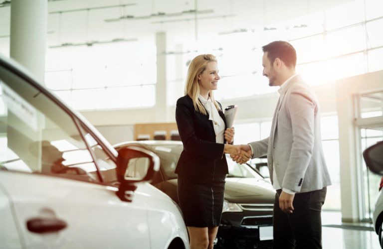 a saleswoman shaking hands with a car buyer at a dealership