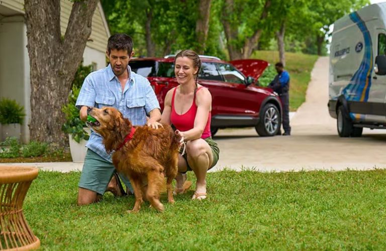 a couple playing with their dog while a Ford technician repairs their car in the background